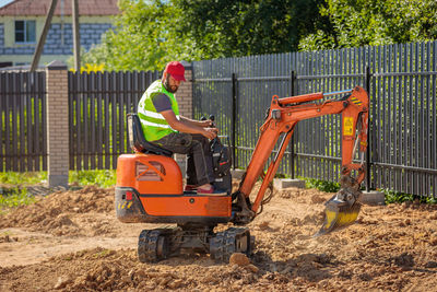 A man on a mini-excavator levels a piece of land, loosens the soil.