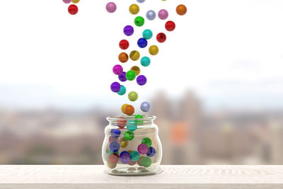 Close-up of colorful balls falling in jar on table against sky