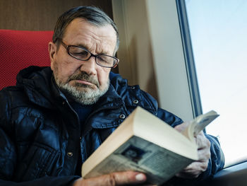 Senior man reading book while traveling in train during winter