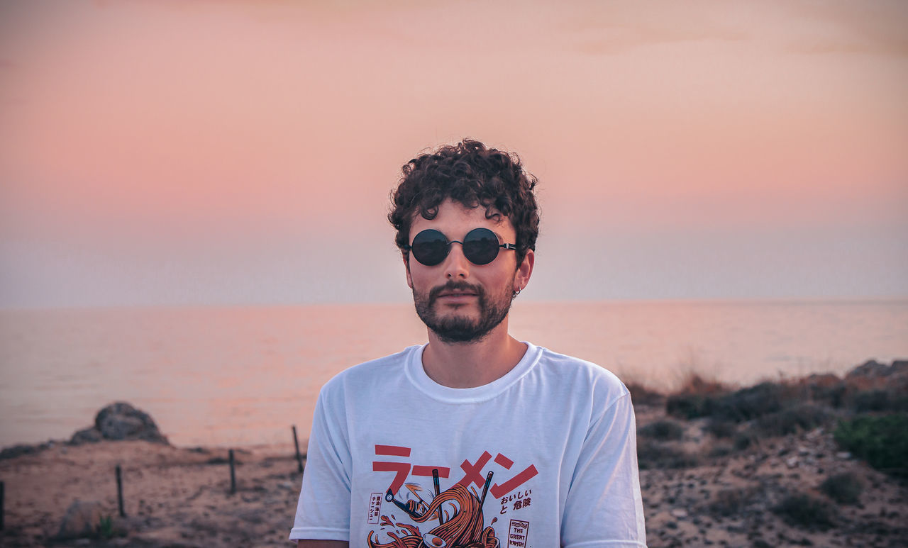 sky, one person, front view, sunset, young men, leisure activity, young adult, portrait, land, lifestyles, focus on foreground, real people, nature, glasses, casual clothing, standing, waist up, sunglasses, outdoors