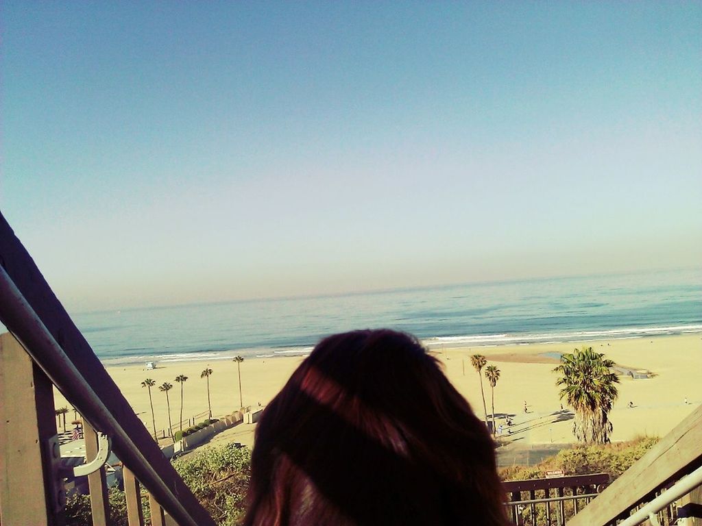 sea, horizon over water, beach, clear sky, lifestyles, water, leisure activity, rear view, person, beauty in nature, shore, scenics, long hair, nature, sky, vacations, railing, tranquility