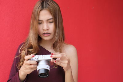 Beautiful young woman holding camera against red background