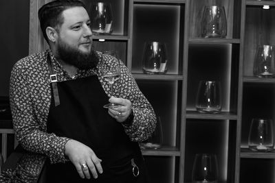 Bartender holding wineglass looking away while standing in bar