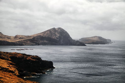 Rock formations on sea against cloudy sky