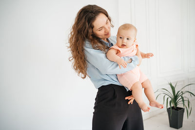 Young mother with long hair and in a shirt holds a newborn daughter. in the arms of a 6 month old 