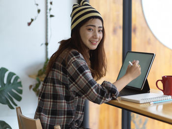 Young woman using digital tablet while sitting on table