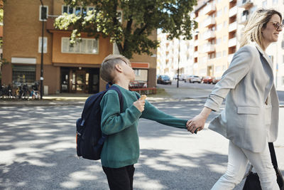 Side view of woman taking stubborn son to school while walking on street