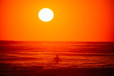 Silhouette man amidst sea against orange sky