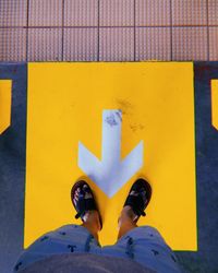 Low section of man standing on yellow arrow sign