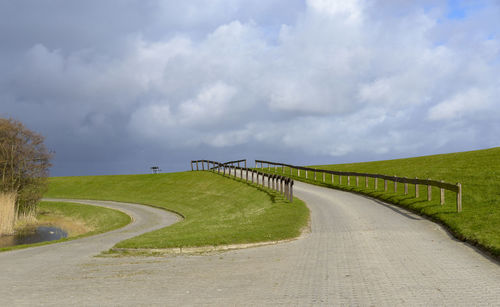 Road leading towards green landscape against sky