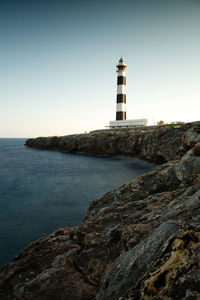 Lighthouse by sea against clear sky