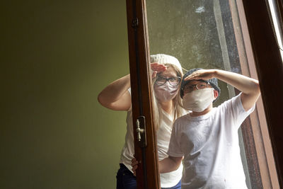 Mother with a child in medical masks looking out the window.