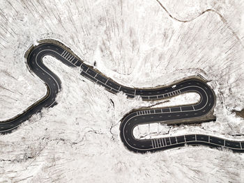 Curvy windy road in snow covered forest, top down aerial view.