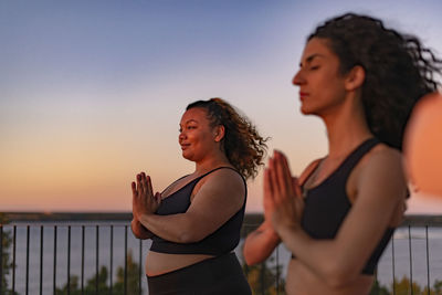 Smiling woman with hands clasped by female friend at sunset