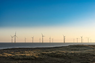 Wind turbines on land by sea against sky