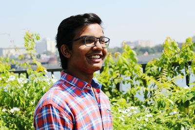 Cheerful young man wearing eyeglasses by plants