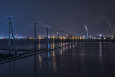 Illuminated city by river against sky at night