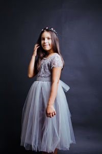 Portrait of girl wearing white dress against black wall