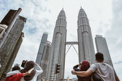 Rear view of people looking at petronas towers against cloudy sky