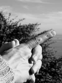 Close-up of hand clasped against sky