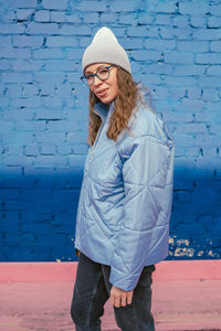 Portrait of young woman standing against wall