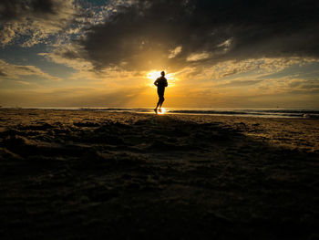 Silhouette person on beach against sky during sunset