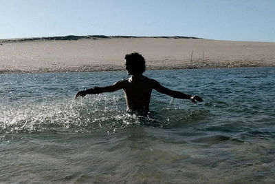 Full length of shirtless man in sea against sky