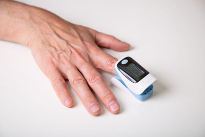 Cropped hand of person holding thermometer against white background