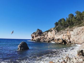 Rock formations in sea against clear blue sky