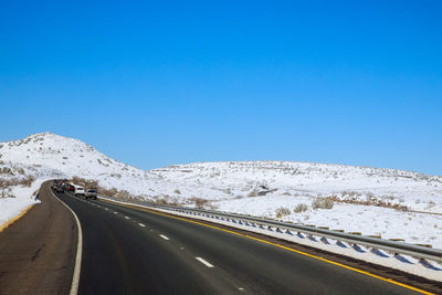 Road leading towards mountains against clear blue sky