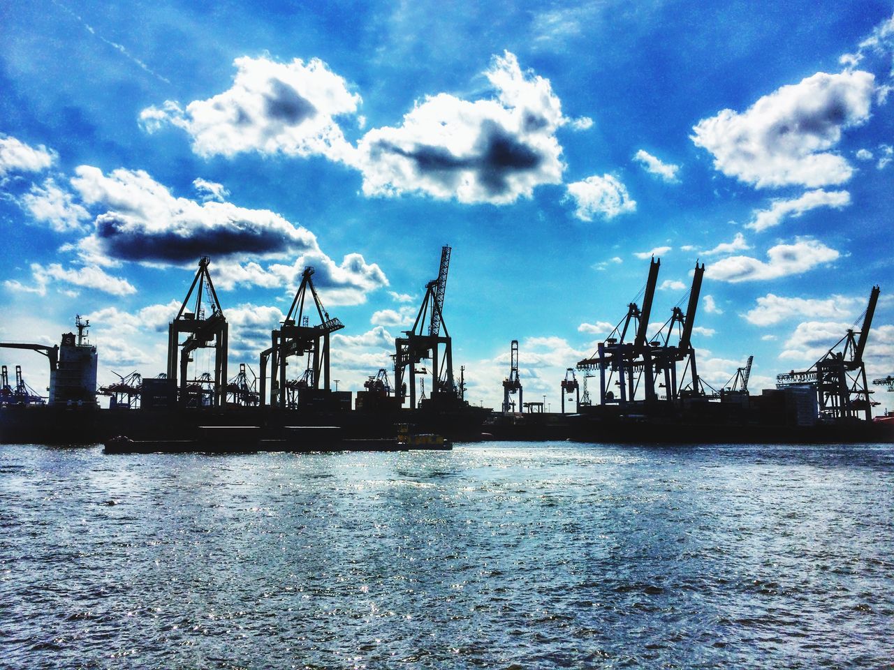 water, sky, waterfront, commercial dock, harbor, sea, cloud - sky, cloud, crane - construction machinery, fuel and power generation, built structure, rippled, crane, nautical vessel, nature, industry, outdoors, blue, no people, shipping