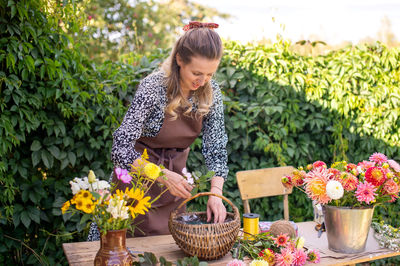 A florist girl collects a bouquet of autumn flowers in a basket on the street