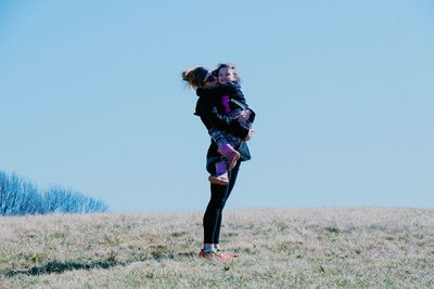 Mother kissing daughter while standing on field against clear sky