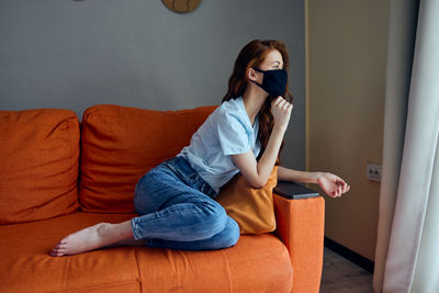 Young woman wearing mask sitting on sofa at home