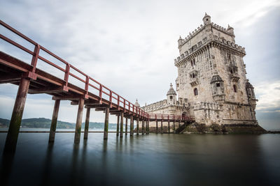Low angle view of bridge over river against cloudy sky