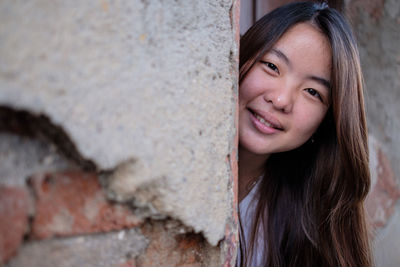 Portrait of smiling young woman standing behind wall
