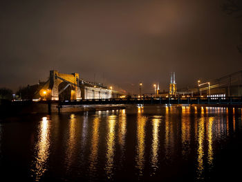 Illuminated bridge over river against sky at night