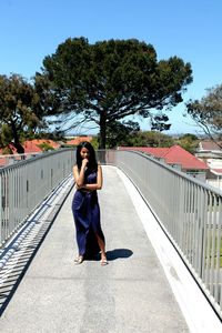 Young woman standing by railing against trees