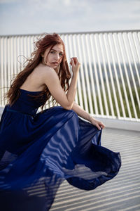 Side view portrait of woman wearing navy blue dress by railing