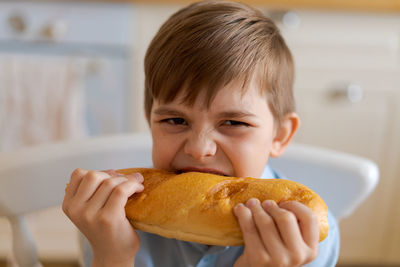 Happy handsome young teenage boy holding and eating freshly baked bread.