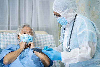 Doctor examining senior woman wearing mask at hospital