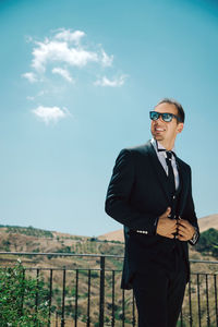 Young man wearing sunglasses standing against sky