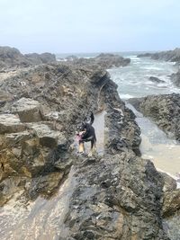 Man on rock by sea against sky