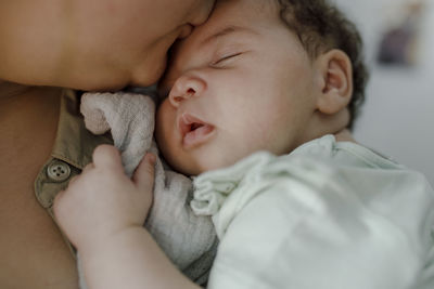 Mother kissing newborn baby girl on forehead at home