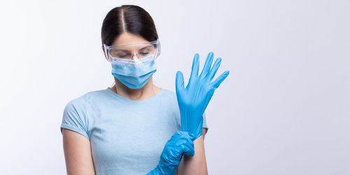 Doctor in mask wearing surgical glove against gray background