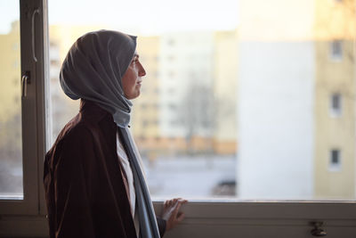 Thoughtful woman in headscarf looking through window