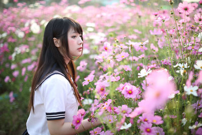 Side view of young woman standing amidst flowering plants