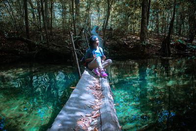 Young woman sitting on log over lake against trees in forest