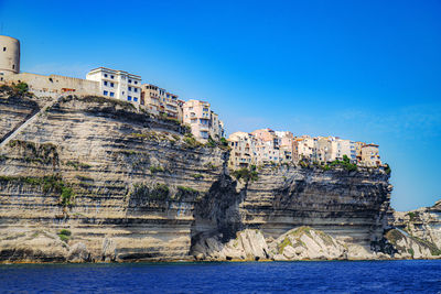 Built structure on cliff by sea against blue sky