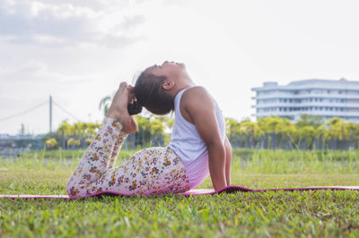 Side view of girl exercising on grassy field against sky